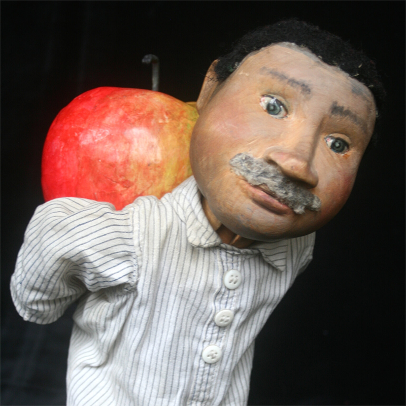 Großfigur mit Schnurrbart und gestreiftem Hemd, einen roten Apfel über der Schulter – Figur aus „JANOSCHs Apfelmännchen“