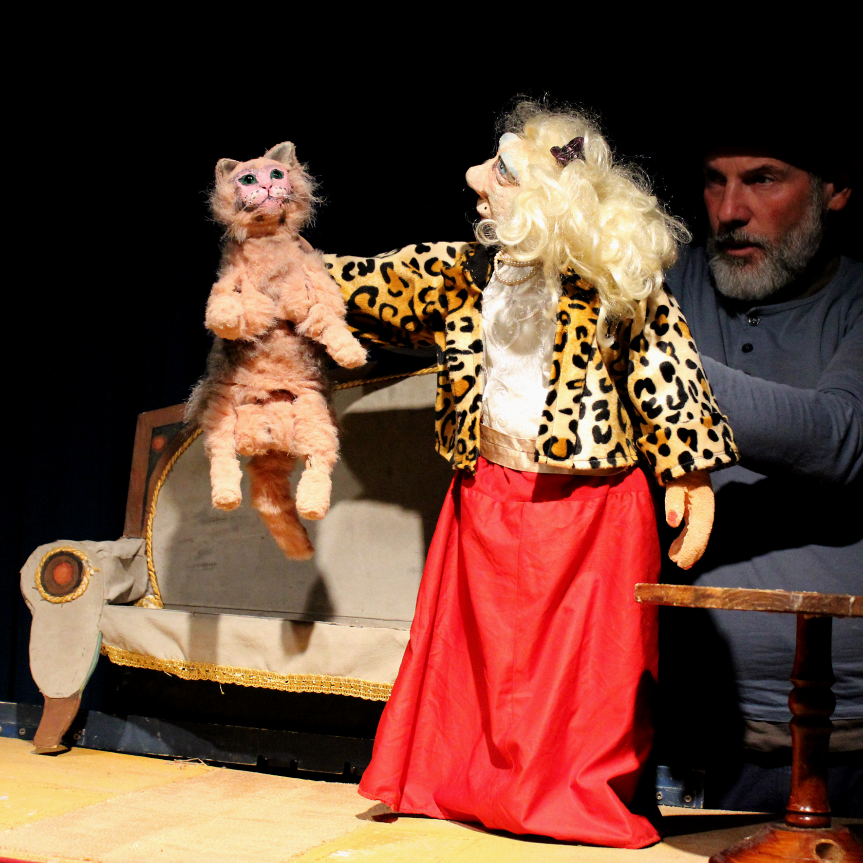 Puppenspielerin im Leopardenjackett mit einer rosa Katzenfigur, dahinter ein Sofa als Kulisse – Szene aus „Die Bremer Stadtmusikanten“
