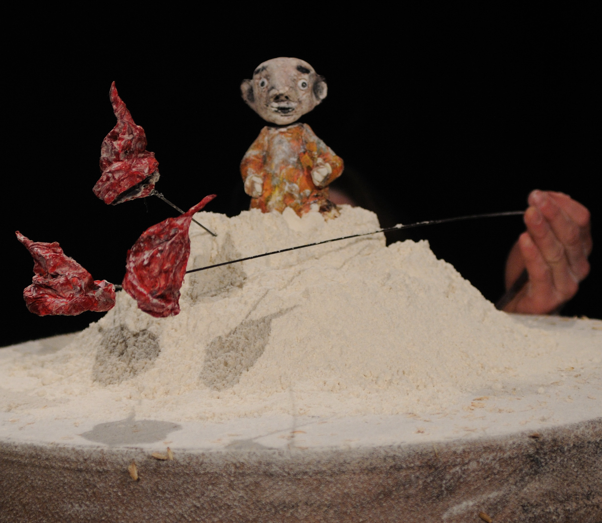 popup_gross Kleine Figur mit Schnauzbart auf einem Sandhügel, daneben rote Stofffetzen an Stäben – Figurenbild aus „Zwergenmützchen“